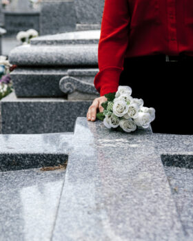 Woman in red blouse putting flowers to a loved one in the cemetery.